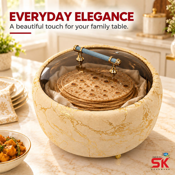 An elegant round tabletop steamer or warmer with a cream marble-patterned exterior and gold detailing, shown on a marble countertop in a bright kitchen. Inside, flatbread or tortillas are stacked on a liner under a clear lid with a blue handle.
