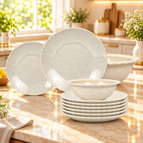 A speckled off-white ceramic dinnerware set arranged on a marble kitchen countertop, including plates, bowls, and a mixing bowl, with a bright kitchen background.