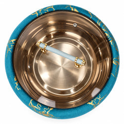 Top-down view of a round metallic bowl with a turquoise blue fabric rim featuring gold leaf patterns, a light blue handle with gold accents, and a brushed copper interior.