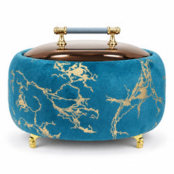 A round velvet box with a metallic blue body and gold marble pattern, featuring a copper-toned lid with a blue-and-gold handle and gold feet, shown on a white background.