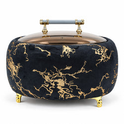A round velvet storage box or basket in black with a gold marble pattern, featuring a glass lid, gold feet, and a light blue handle on a white background.