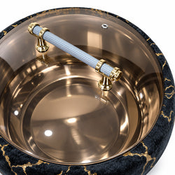 A close-up of a round metallic bowl or tray with a brushed copper interior, a ribbed silver-and-white handle with gold-toned hardware, and a dark blue velvet rim with gold marbled veining, shown on a white background.