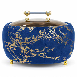 A round velvet ottoman or stool in deep blue with an intricate gold marble vein pattern, featuring a matching blue velvet lid with gold metal hardware and small gold feet.