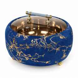 A round decorative bowl or ashtray with a deep blue velvet exterior featuring gold abstract branch-like patterns, a reflective metallic interior, and a glass top lid supported by gold hardware.
