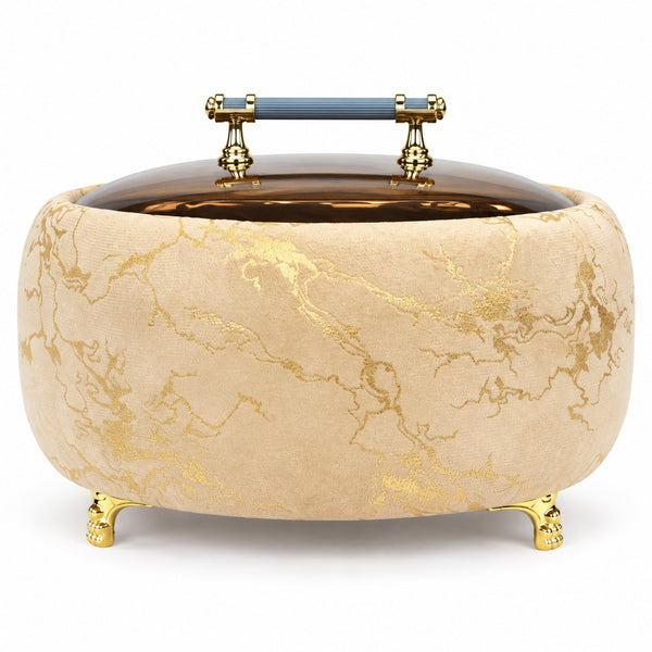 An ornate round storage box or trunk with a beige velvet exterior featuring gold marble-like veining, a dark brown glass or acrylic lid, gold feet, and a blue-and-gold handle on a white background.